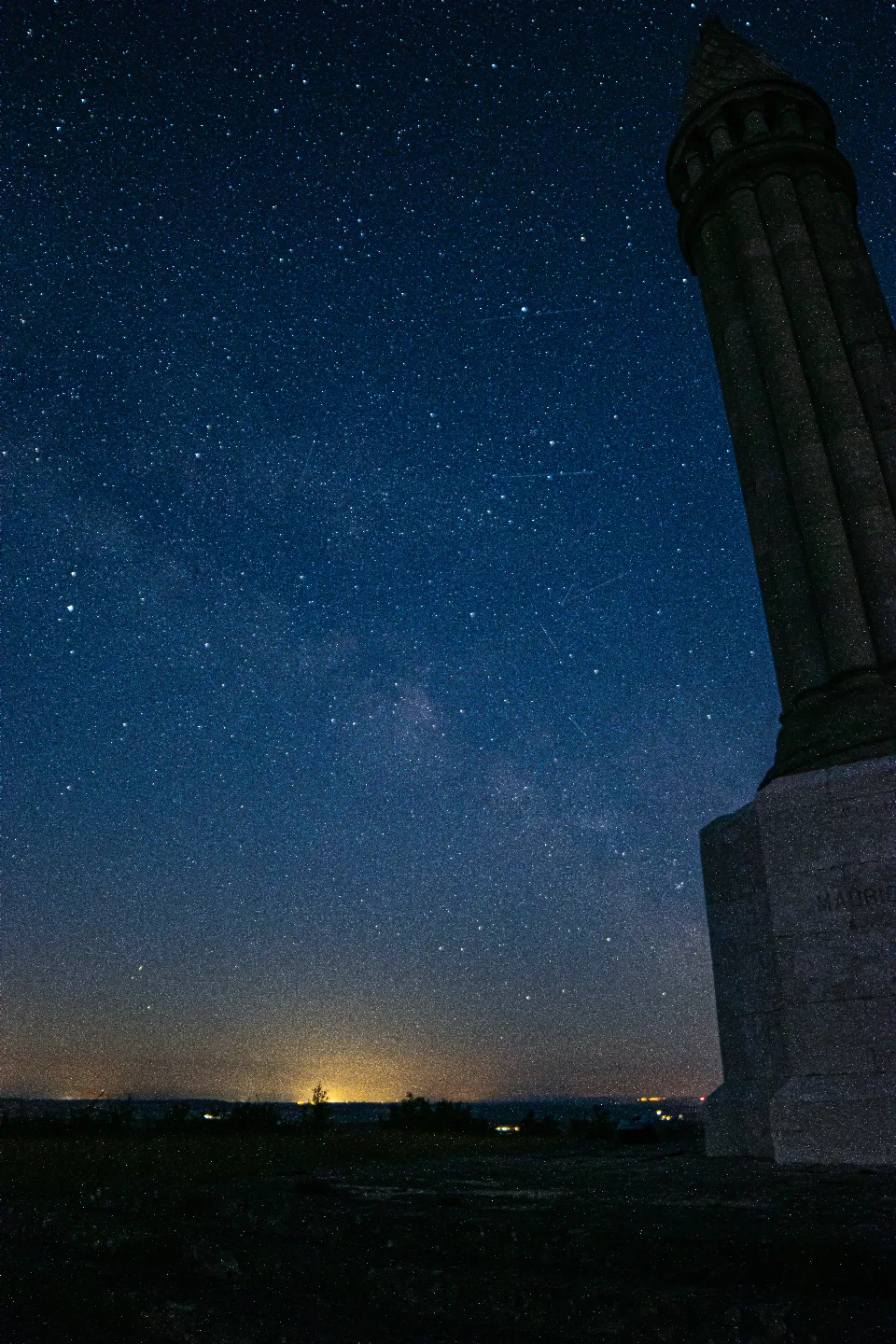 Milchstraße und zahlreiche Sterne über einem beleuchteten, runden Steinturm in Nancy, Frankreich.